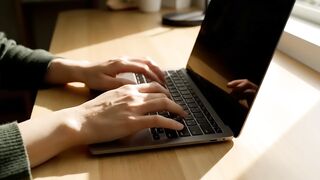 Close-up of Person Typing on Laptop at Wooden Desk in Sunlight