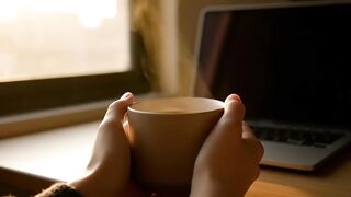 Hands Holding Steaming Mug in Warm Home Office