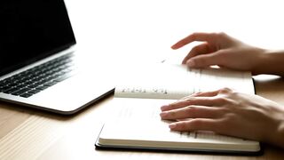 Professional Workspace with Hands Planning in Notebook Next to Laptop