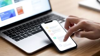 Close-up of Person Using Smartphone for App Navigation Next to Laptop on Desk