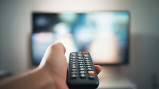Hand Holding TV Remote Control to Blurred Screen