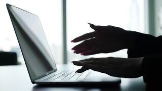 Silhouetted Hands Typing on Laptop in Bright Office