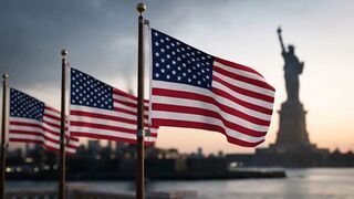 American flags waving in the wind with the Statue of Liberty standing in the distance background
