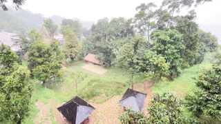 Rain over a green park with two gazebos in the foreground and a traditional hut in the middle ground, on a cloudy day