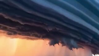 Dark storm clouds forming over farmland with glowing sunset light on the horizon.