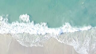 Aerial view of the beautiful turquoise waves crashing on the sand beach with white umbrellas