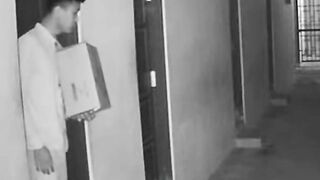 Young Man Receiving Cardboard Package in Apartment Hallway CCTV Style