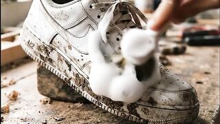 Hand cleaning dirty white sneakers with foam brush on wooden workbench for restoration process