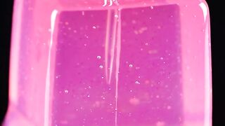 Pink liquid pouring into clear plastic container with splashing droplets and glossy texture