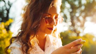 Happy Curly Woman Enjoying Sunny Day While Using Her Phone