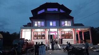 The exterior of a mosque featuring Chinese-style architecture and bright lighting at dusk, as residents arrive for worship.
