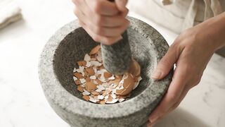 A WOMAN CRUSHING EGGS TO MAKE VIM FOR CLEANING PLATES