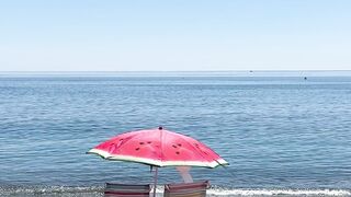 Serene beach view with chairs and a red umbrella, perfect for a relaxing day.