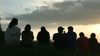 7 friends sitting together, enjoying the evening sunset in the area around the rice fields