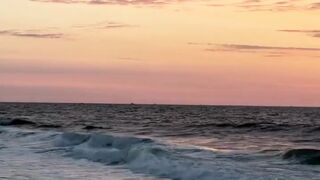 Ocean waves crashing on sandy shore under colorful pink and orange twilight sunset sky