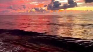 Ocean waves crashing on beach shore under dramatic red and orange sunset sky
