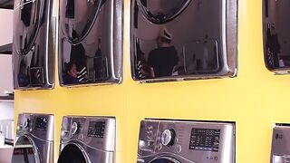 A row of modern, front-loading washing machines and dryers installed against a yellow wall