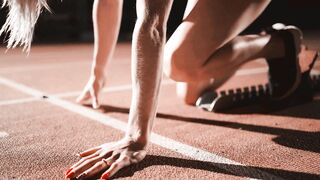 Female Athlete Preparing to Start a Sprint Race in a Dark Stadium