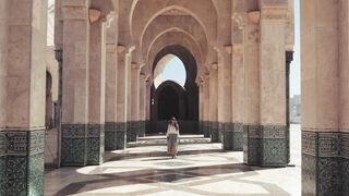 A Woman Walking On A Facade of Concrete Pillars And Arches