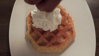 A Person Putting Whipped Cream on top of the Waffle
