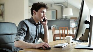 A Young Man Talking On The Phone Working ON Computer