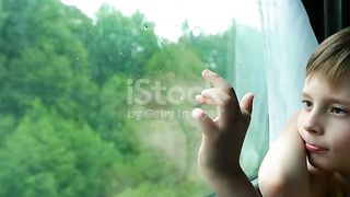 A handsome boy looking outside and enjoy rain drops