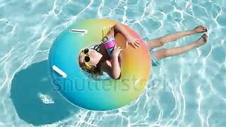 Happy kid playing with colorful swim ring in swimming pool on summer day