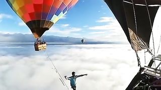 A tightrope walker walks along a cable fixed on both sides to balloons a few kilometers above ground level.